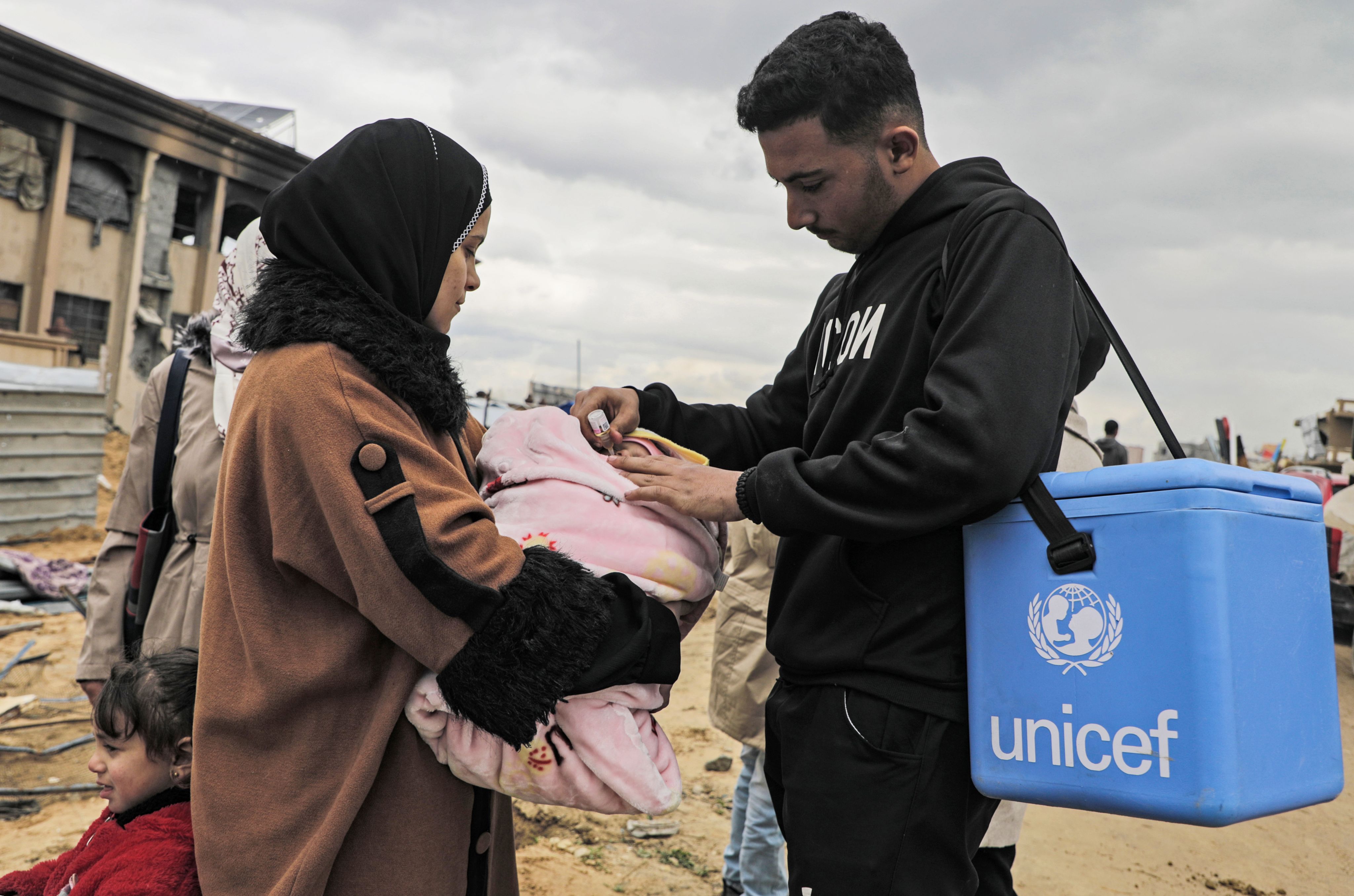 Una madre sostiene a su bebé mientras un trabajador de UNICEF le administra la vacuna contra la poliomielitis en Yabalia, al norte de la Franja de Gaza, en el marco de la campaña de vacunación impulsada por el Ministerio de Salud palestino con el apoyo de la OMS, el UNICEF y el OOPS para poner fin al brote.