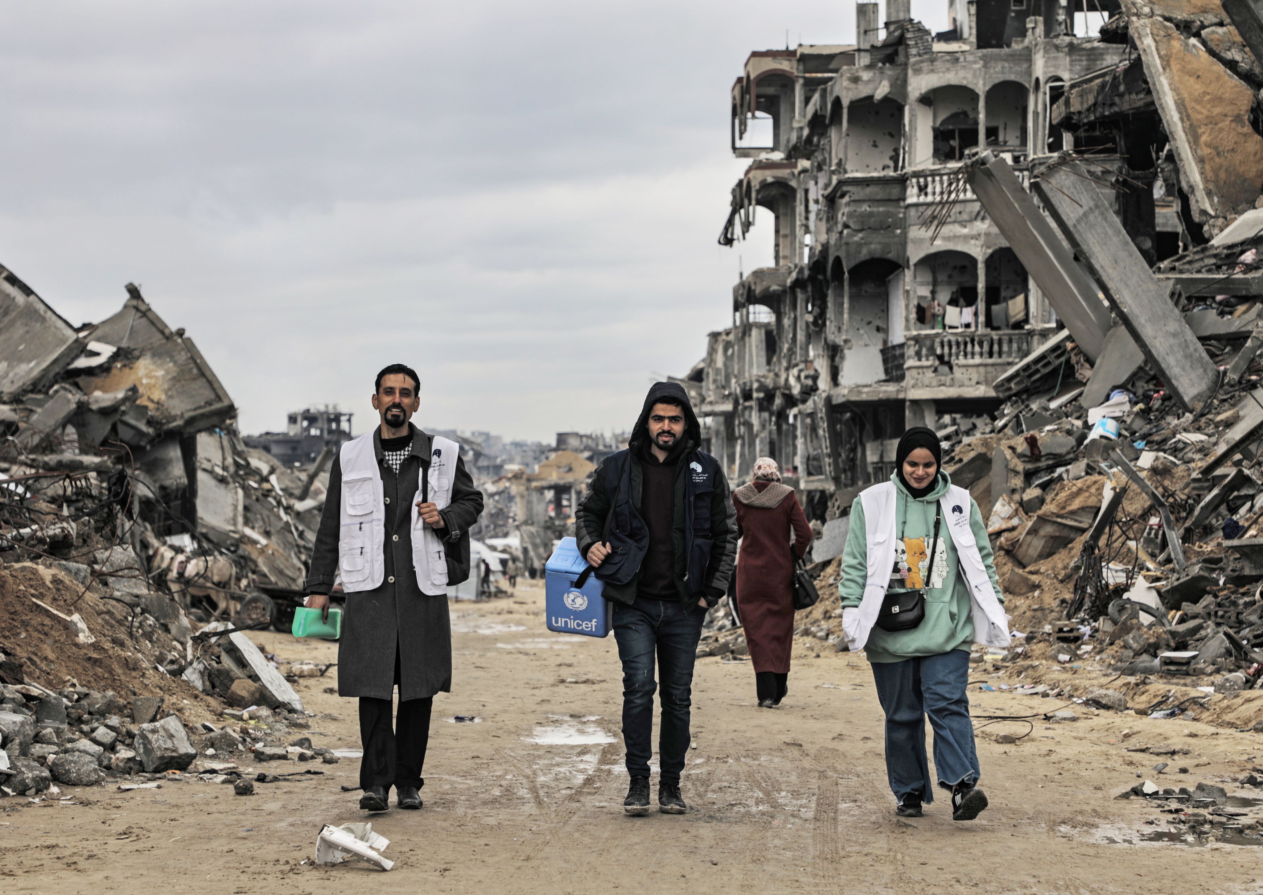 Tres integrantes de un equipo móvil de vacunación recorren una calle en ruinas de Yabalia, al norte de la Franja de Gaza, con el material necesario para administrar las vacunas contra la poliomielitis.